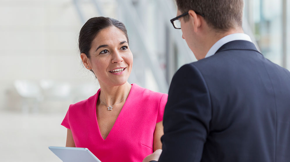 Business woman in pink suit dress talking to a business man over an tablet.