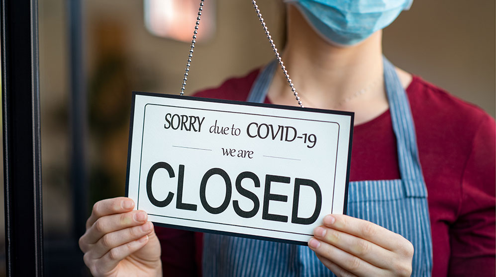 Retailer turning a door sign to: "SORRY due to COVID-19 we are CLOSED"