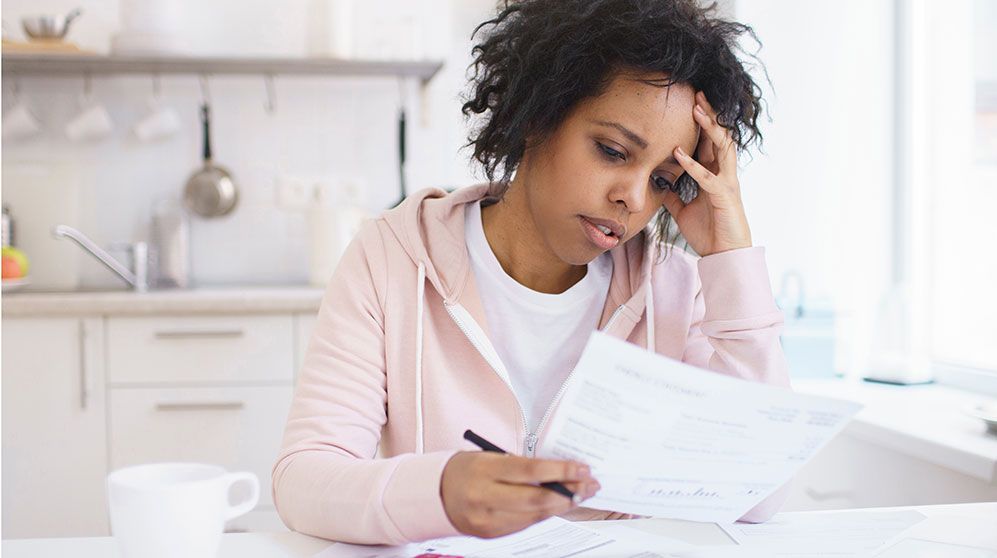 Woman working on bills in kitchen looking worried.