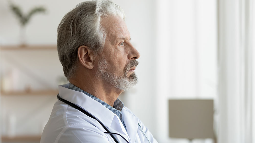 Older man looking worried out a bright window.