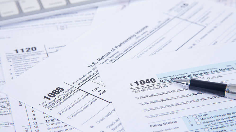 Top of tax forms 1040, 1065, 1120 fanned on a table.