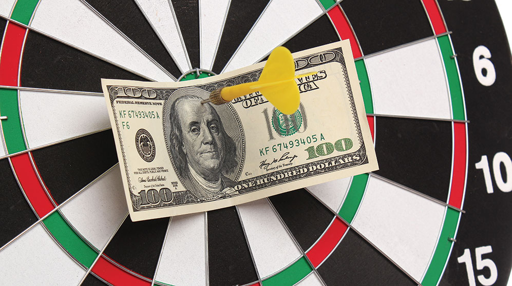 A $100 bill stuck by a yellow dart in the bullseye of dart board.