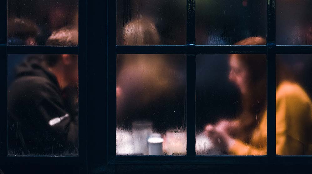 Hazy view of couple dining through leaded glass windows.