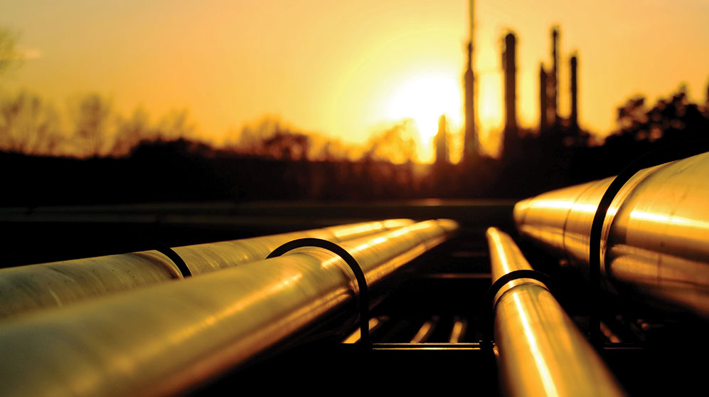 Four pipelines leading into a refinery silhouetted by setting sun.