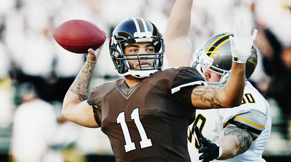 Quarterback with arm back about to throw with defender about to tackle from behind