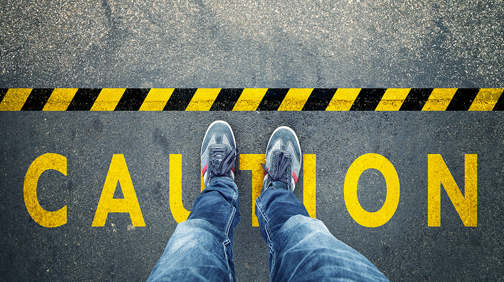 legs of a person standing over the word caution framed by yellow and black warning tape